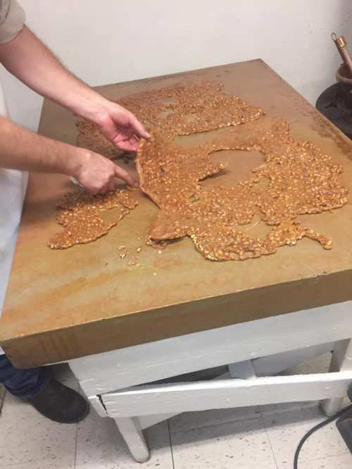 A person spreads a layer of freshly made candy on a large, flat surface.
