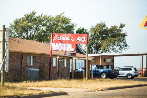 A vintage motel sign reading "Fabulous 40" with "Vacancy" displayed, surrounded by trees and parked cars.