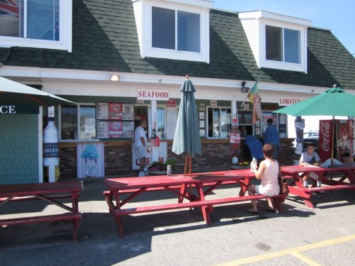 A seafood restaurant with outdoor seating, featuring a menu board and umbrellas, on a sunny day.