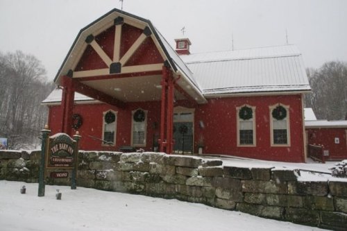 A red building with a white roof and snow falling, featuring a sign that reads "The Barn" in a winter landscape.