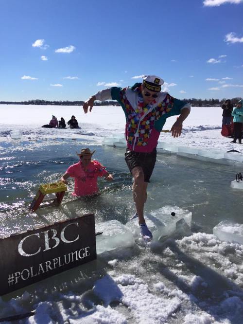 A person in a colorful outfit jumps into icy water during a polar plunge event, with spectators in the background.