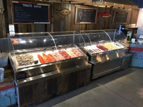 Display of fresh seafood in glass cases at a market, featuring various fish and shellfish options.