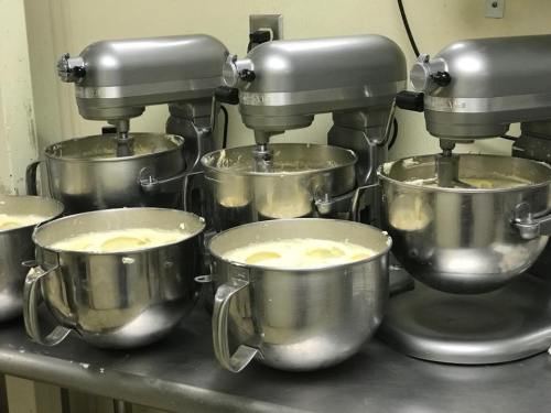 A row of silver stand mixers with bowls filled with batter on a kitchen countertop.