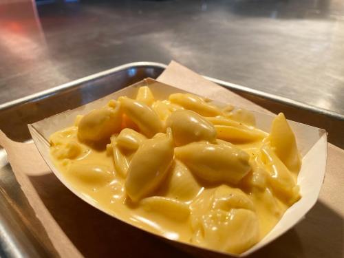A serving of creamy macaroni and cheese in a paper tray on a metal surface.