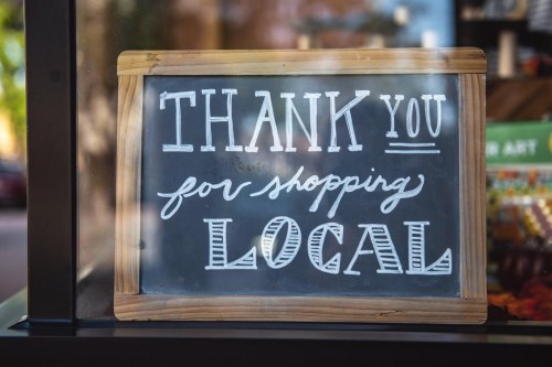 Chalkboard sign that reads "Thank you for shopping local" in decorative white lettering on a wooden frame.