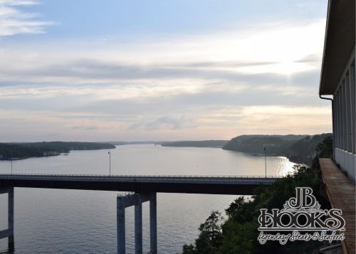 A serene view of a bridge over a calm river, with soft clouds and a sunset in the background.