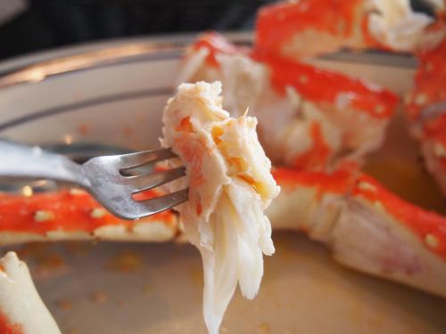 A fork holding a piece of crab meat, with crab legs in the background on a plate.