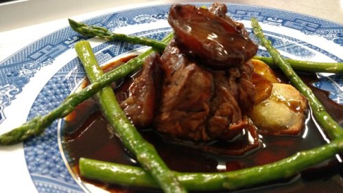 A plated dish featuring tender beef, asparagus, and a rich sauce on a decorative blue and white plate.