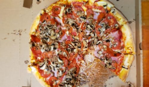 A large pizza topped with pepperoni, mushrooms, and other ingredients, partially eaten, in a cardboard box.
