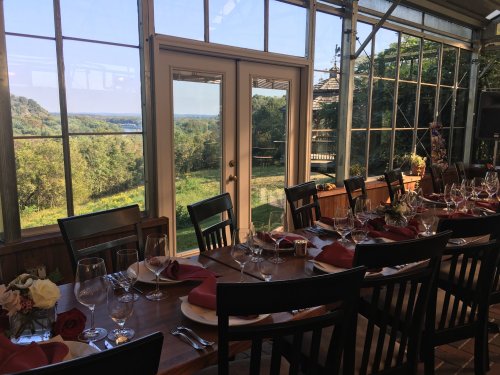 A beautifully set dining table with wine glasses and red napkins, overlooking a scenic view through large glass windows.