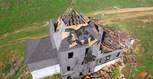 Aerial view of a dilapidated building with a missing roof and scattered debris in a grassy area.