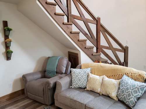 Cozy living space featuring a gray couch with decorative pillows, a recliner, and a wooden staircase.