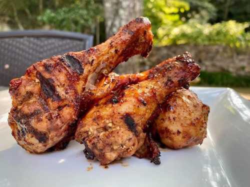 Grilled chicken drumsticks with a smoky glaze, served on a white plate against a blurred outdoor background.