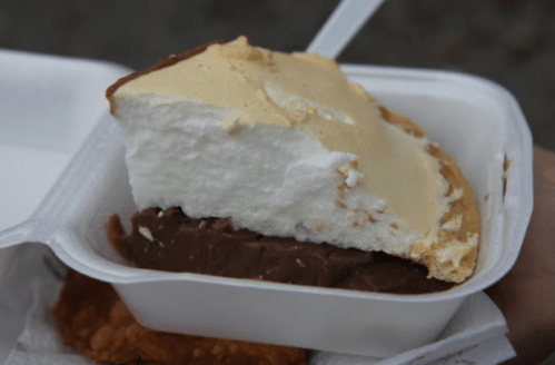 A slice of chocolate pie topped with fluffy meringue, served in a white takeout container.