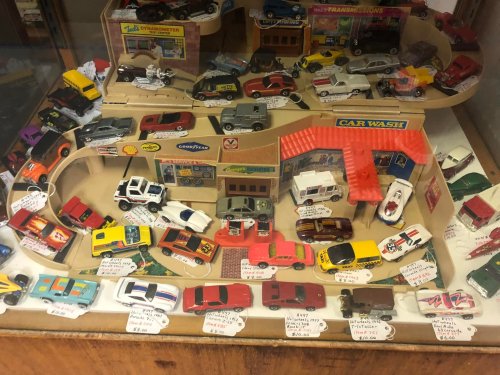 A display case filled with various toy cars and a car wash model, labeled with prices and descriptions.