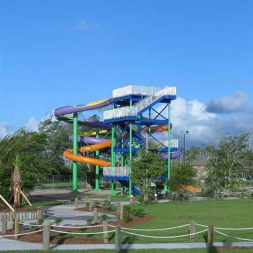 Colorful water slides tower over a grassy area under a blue sky, with trees and pathways nearby.