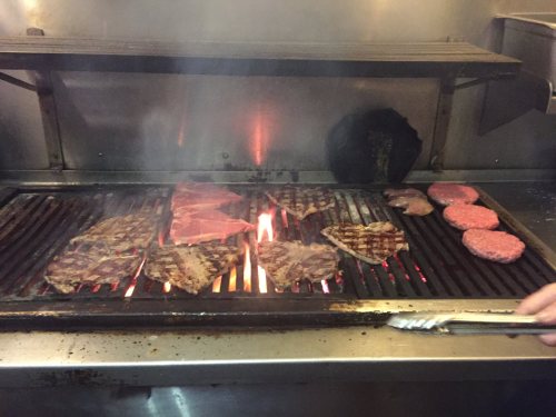 Grilling various meats on a barbecue, with smoke rising and flames visible between the cuts.