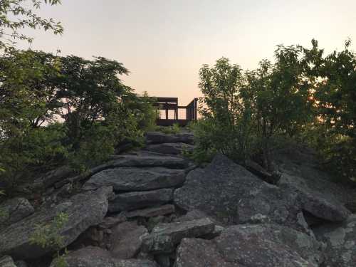 A rocky path leads to a wooden lookout structure surrounded by greenery at sunset.