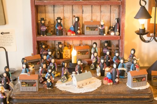 A display of colorful wooden figurines arranged on shelves, depicting a market scene with various stalls and a small house.