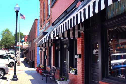 A charming street scene featuring brick buildings with striped awnings, flower pots, and parked cars under a clear blue sky.