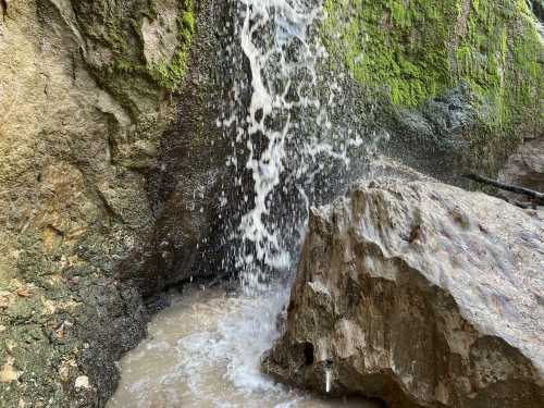 A small waterfall cascades over moss-covered rocks into a shallow pool below.