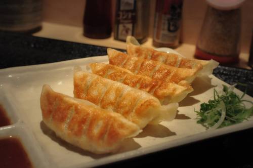A plate of golden-brown gyoza dumplings served with dipping sauce and garnished with green onions.