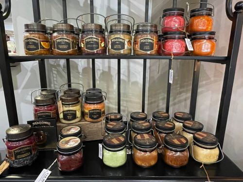 A display of various jars filled with colorful preserves and sauces on a black shelf.
