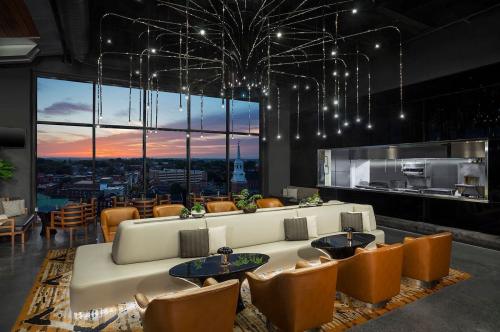 Modern lounge with a white sofa, brown chairs, and a stunning sunset view through large windows. Elegant lighting fixtures above.