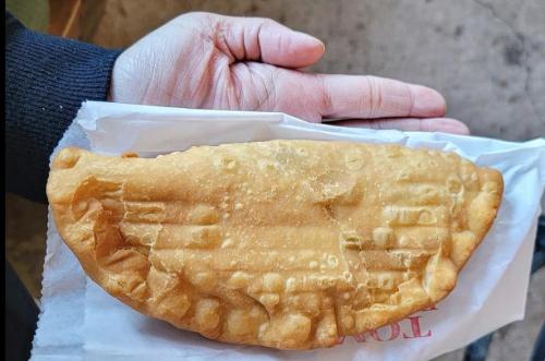 A hand holding a large, golden-brown fried pastry on a white paper wrapper.