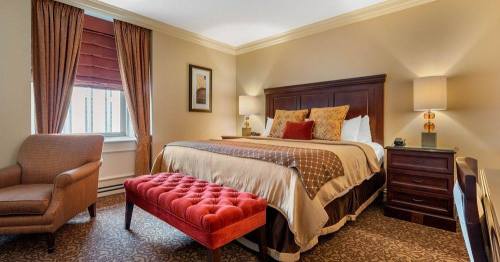 Cozy hotel room featuring a king bed, armchair, ottoman, and warm lighting with elegant decor.
