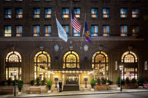 Historic hotel entrance with flags, large arched windows, and a doorman in front, illuminated at night.