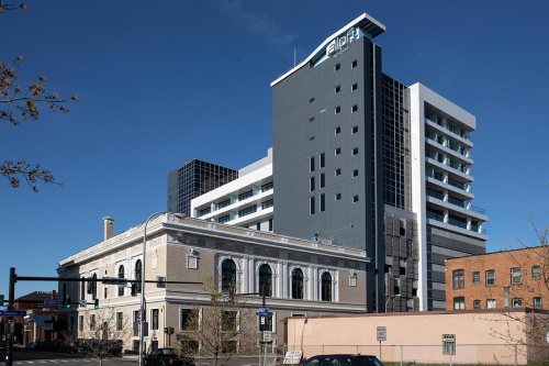 Modern high-rise building next to a historic structure, set against a clear blue sky. Urban cityscape.
