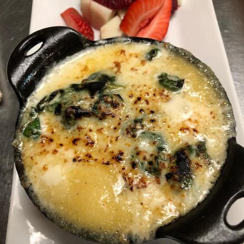A creamy, baked dish with a golden top, served in a small cast-iron skillet, alongside fresh strawberries and fruit.