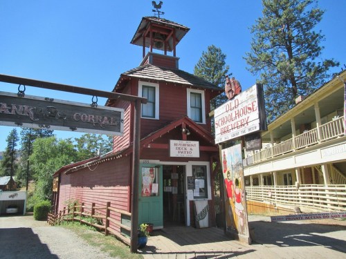 A red wooden building with a clock tower, featuring signs for a restaurant and an old schoolhouse, surrounded by trees.