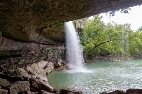 A waterfall cascades from a rocky overhang into a serene green pool surrounded by lush vegetation.