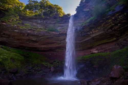 A serene waterfall cascades down rocky cliffs, surrounded by lush greenery and a tranquil pool below.