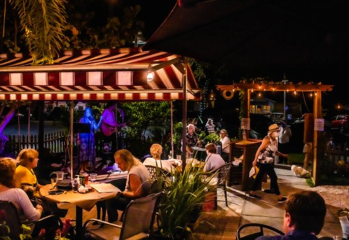 A lively outdoor restaurant scene at night, with diners enjoying food and live music under colorful awnings.