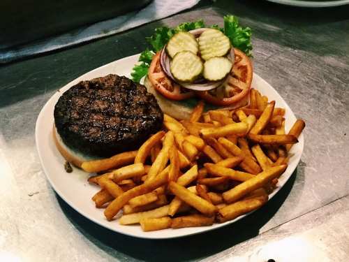 A plate with a grilled burger patty, fresh toppings, and a side of golden French fries.