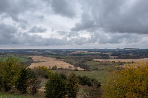 A scenic landscape featuring rolling hills, fields, and a cloudy sky, showcasing autumn colors in the foreground.
