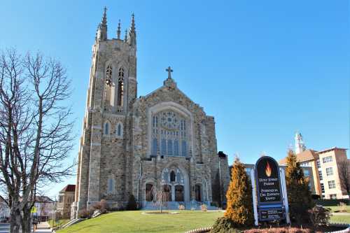 A large stone church with a tall tower and stained glass windows, surrounded by green grass and trees under a clear blue sky.