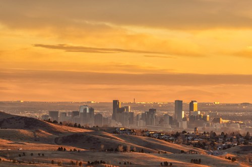 Sunset view of a city skyline with rolling hills in the foreground, bathed in warm golden light.