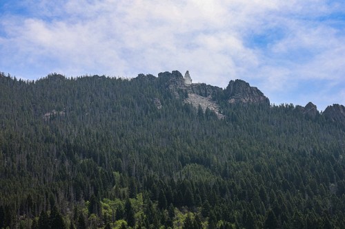 A distant view of a rocky mountain peak covered in trees under a partly cloudy sky.