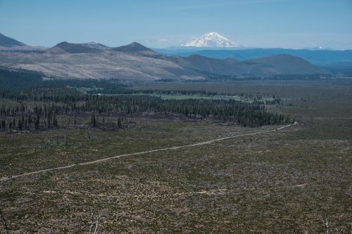 A vast landscape of rolling hills and valleys, with a snow-capped mountain in the distance under a clear blue sky.