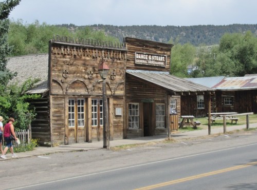 A rustic wooden building with a sign reading "Dance & Stuart General Merchandise" beside a quiet road.