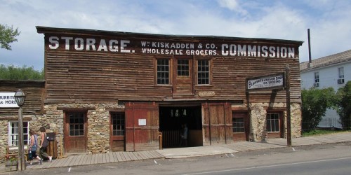 Historic wooden building with a sign reading "Storage W. Kiskadden & Co. Wholesale Grocers" in a rural setting.