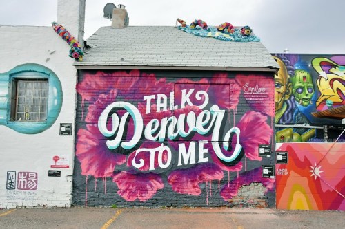 Colorful mural on a building featuring the text "Talk Denver to Me" surrounded by vibrant floral designs.