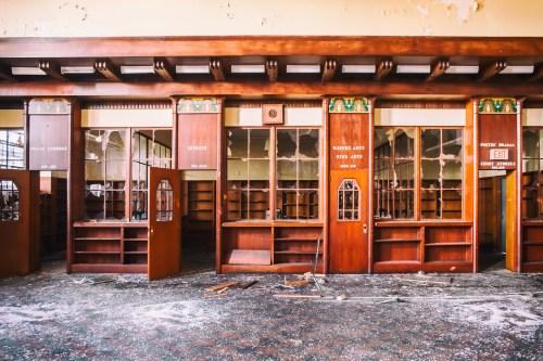 Abandoned library interior with wooden shelves, dusty floors, and peeling paint, showcasing empty bookcases.