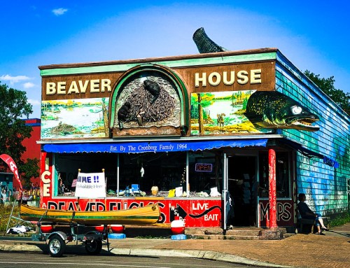 Colorful storefront of "Beaver House," featuring a bear and fish sculpture, with a canoe outside and an open sign.