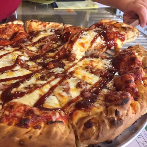 A close-up of a cheesy pizza with barbecue sauce being served from a tray.
