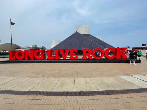 Red letters spelling "LONG LIVE ROCK" in front of a modern building with a pyramid-shaped roof.